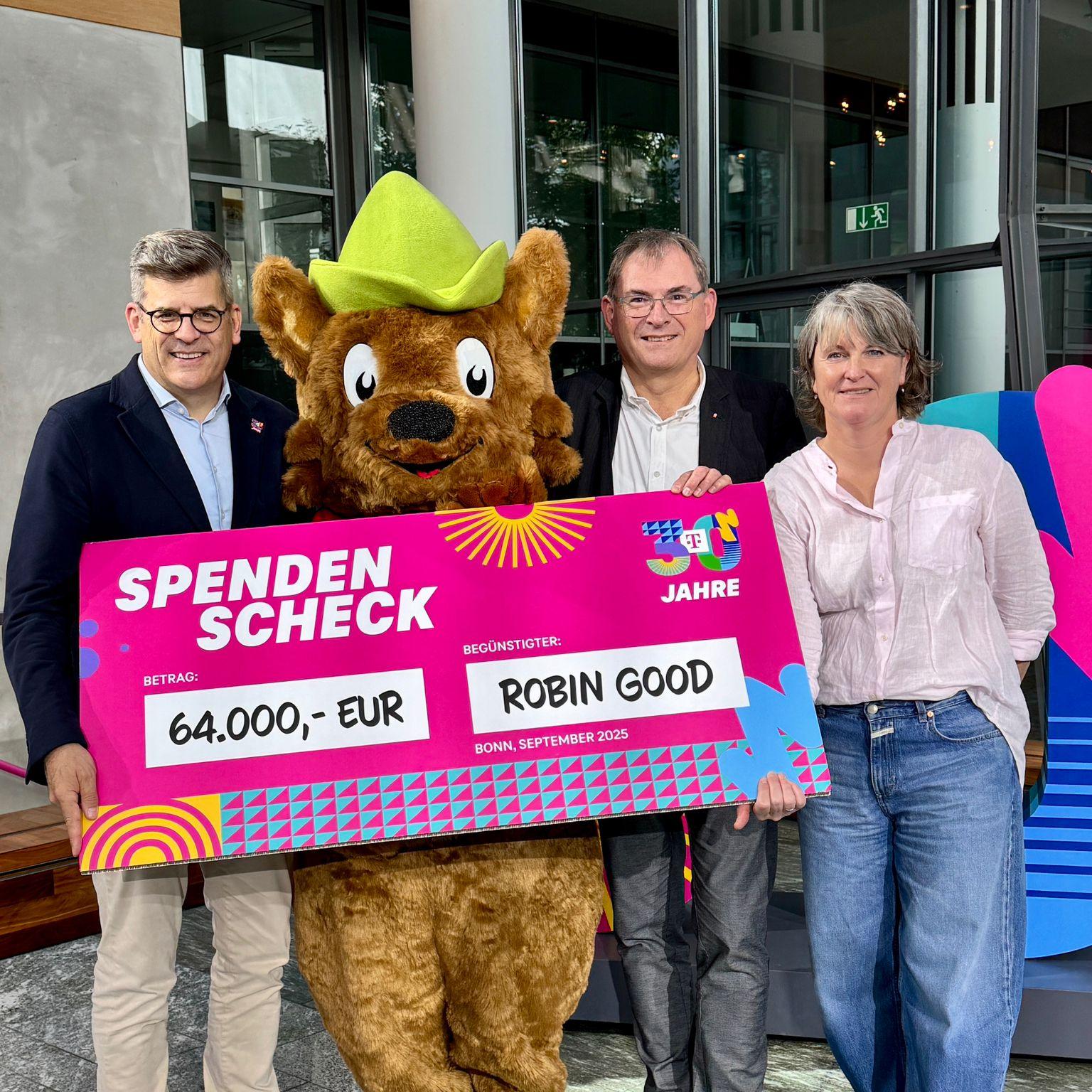 Philipp Schindera (Deutsche Telekom), Maskottchen Robbie, Caritasdirektor Jean-Pierre Schneider und Andrea Elsmann (Diakonie Bonn und Region) halten gemeinsam einen großen Spendenscheck über 64.000 Euro für den Familienfonds Robin Good.
